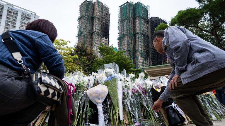 Menschen legen Blumen vor den zerstörten Hochhäusern in Hongkong nieder