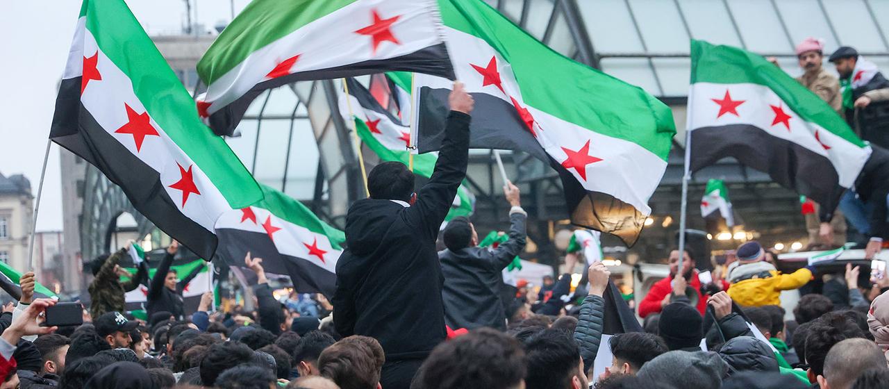 Zahlreiche Menschen schwenken syrischen Flaggen vor dem Hamburger Hauptbahnhof.