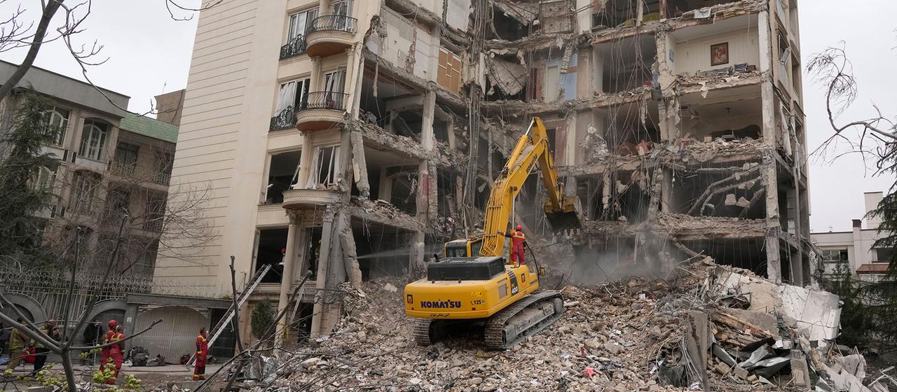 Feuerwehrleute räumen in Teheran mit einem Bagger die Trümmer eines Wohnhauses.