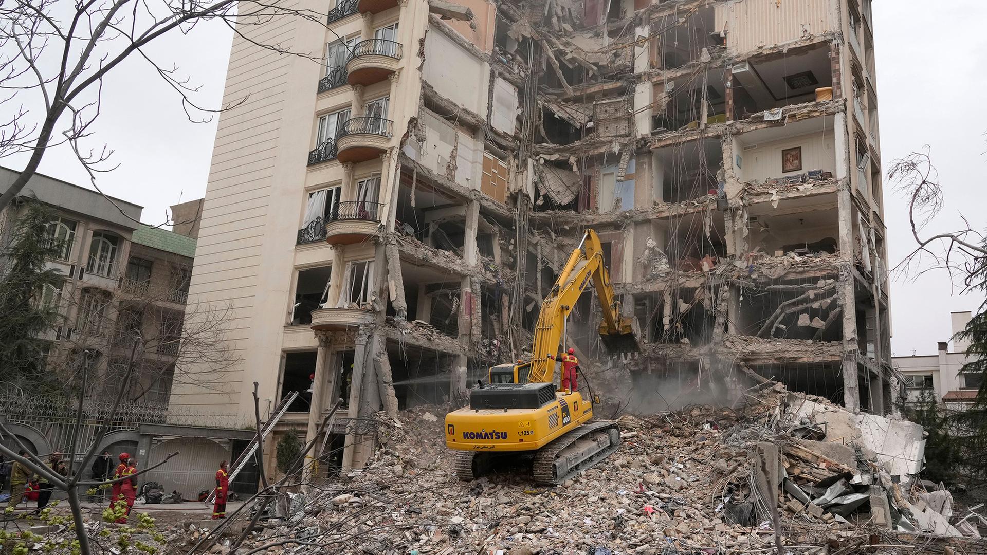 Feuerwehrleute räumen in Teheran mit einem Bagger die Trümmer eines Wohnhauses. | Vahid Salemi/AP/dpa