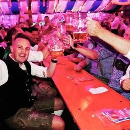 Eine Gruppe Menschen in einem Bierzelt, jeder hält einen Maßkrug hoch