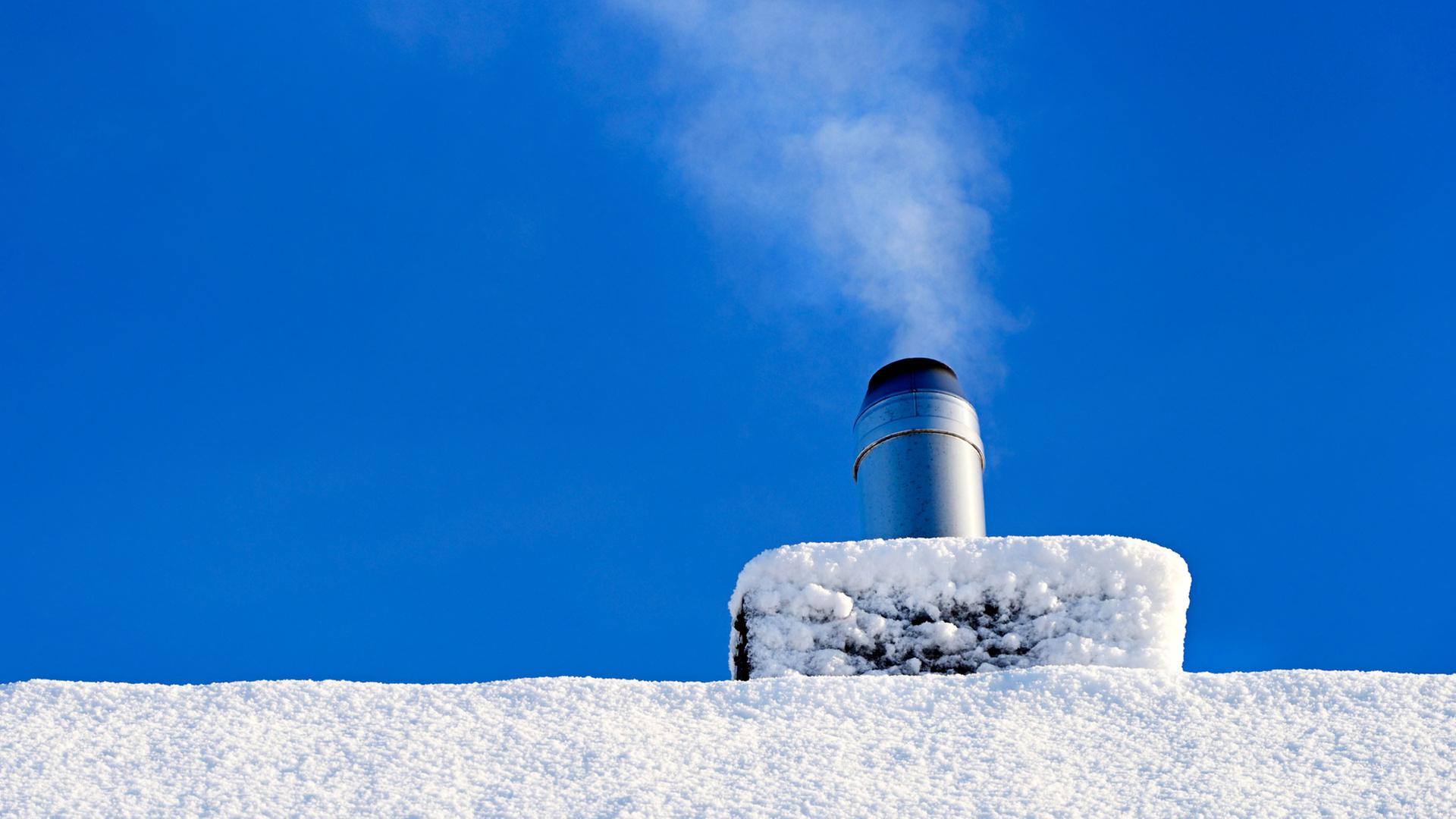 Rauchender Schornstein eines Wohnhauses im Winter. | picture alliance / CHROMORANGE