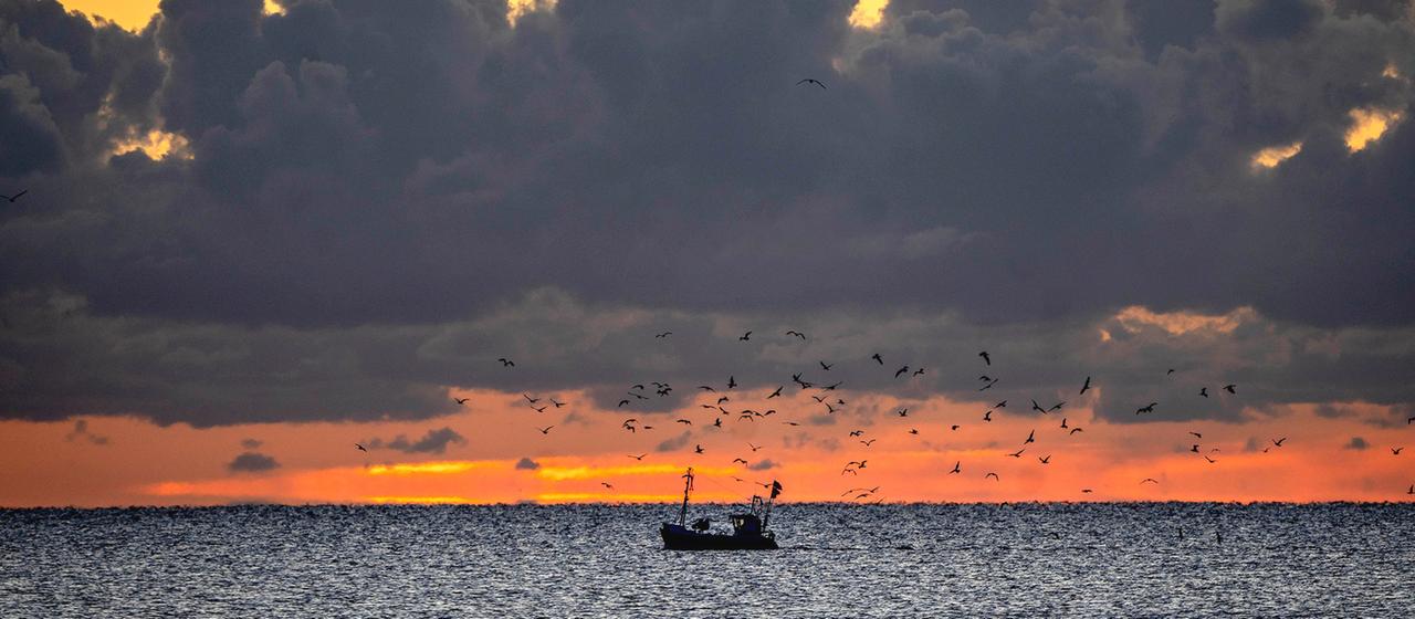 Ein Fischer steuert sein kleines Boot vor Sonnenaufgang über die Ostsee vor Timmendorfer Strand.