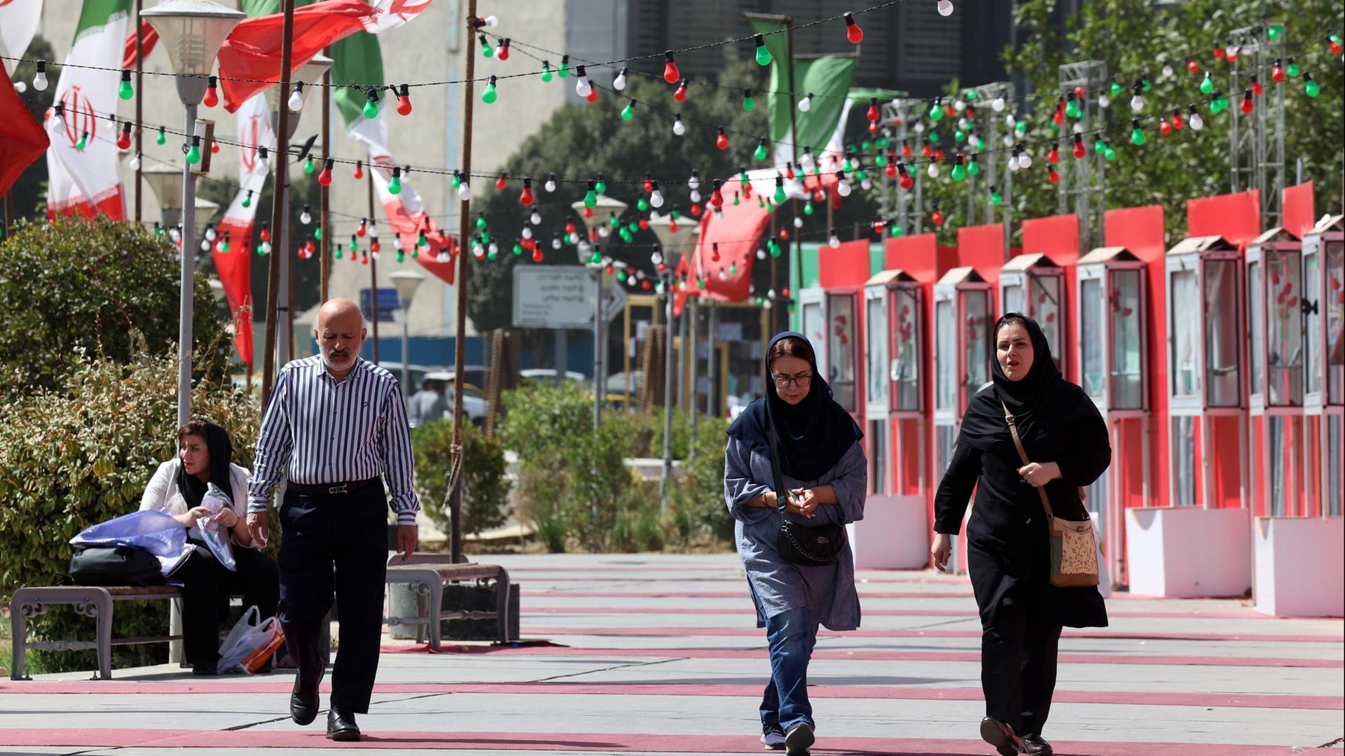 Ein Mann und Frauen laufen in Teheran an iranischen Flaggen vorbei. | EPA