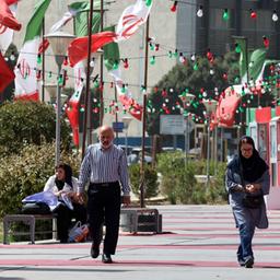 Ein Mann und Frauen laufen in Teheran an iranischen Flaggen vorbei.