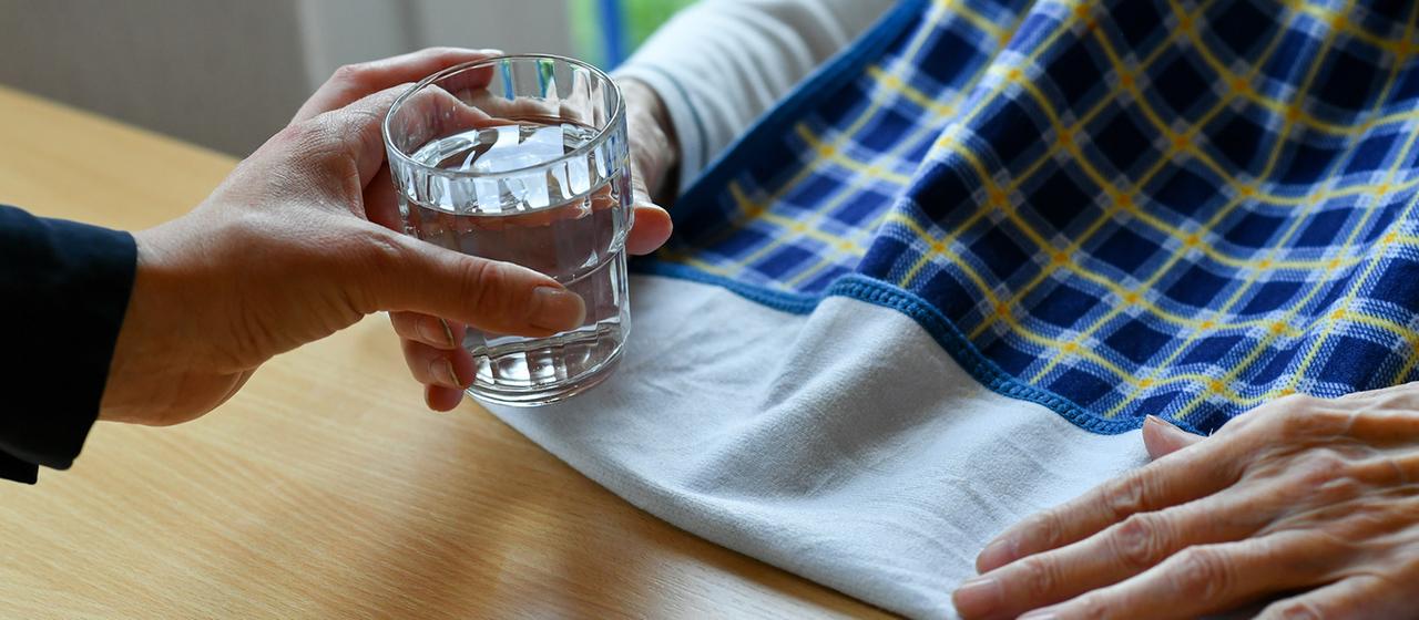 Eine Pflegerin reicht einer alten Frau ein Glas Wasser.