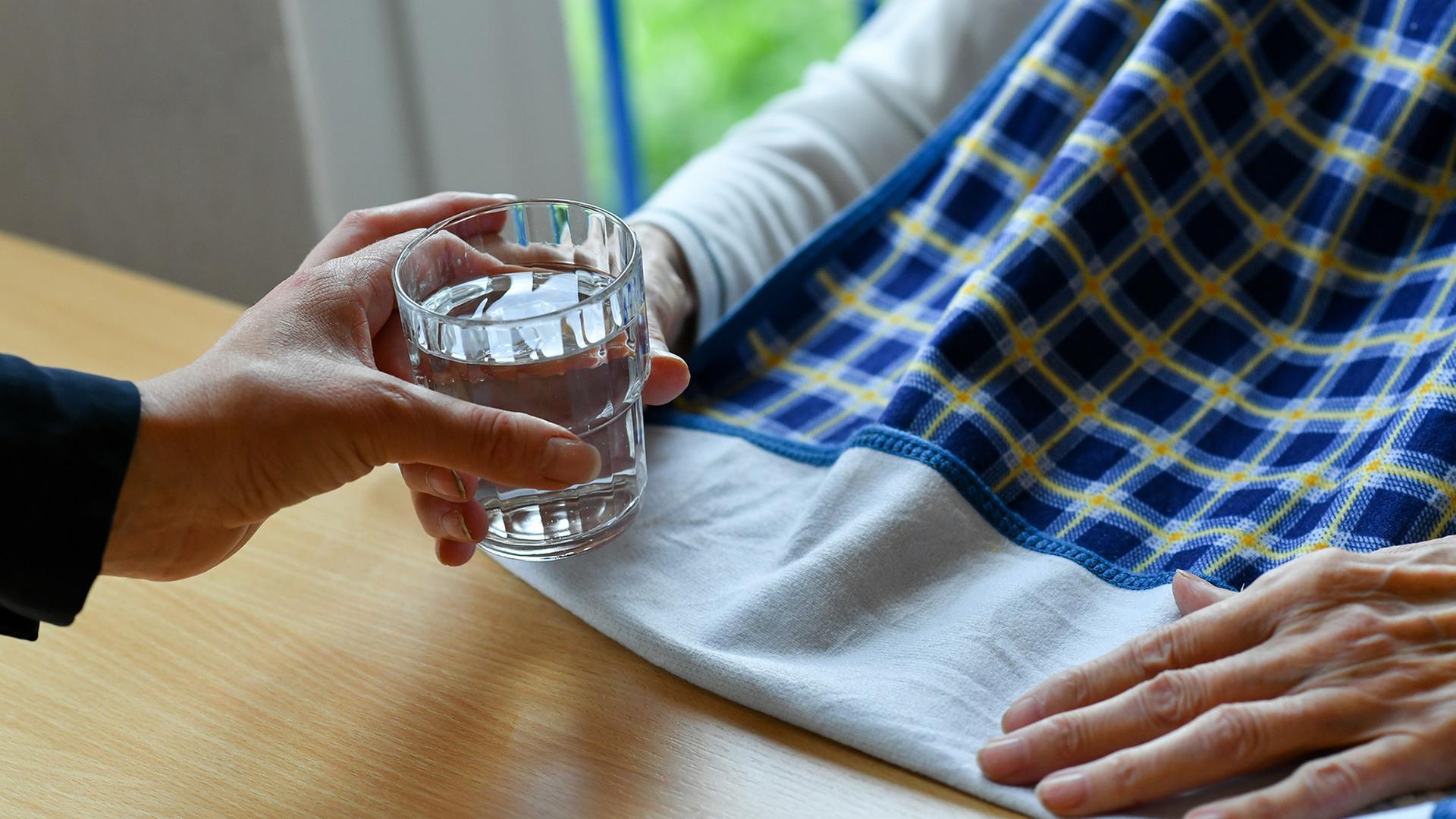Eine Pflegerin reicht einer alten Frau ein Glas Wasser. | dpa