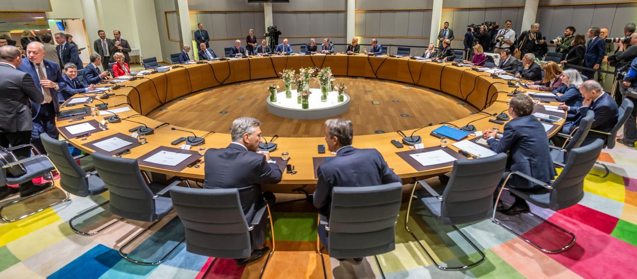 EU heads of state and government sit and stand at a round table