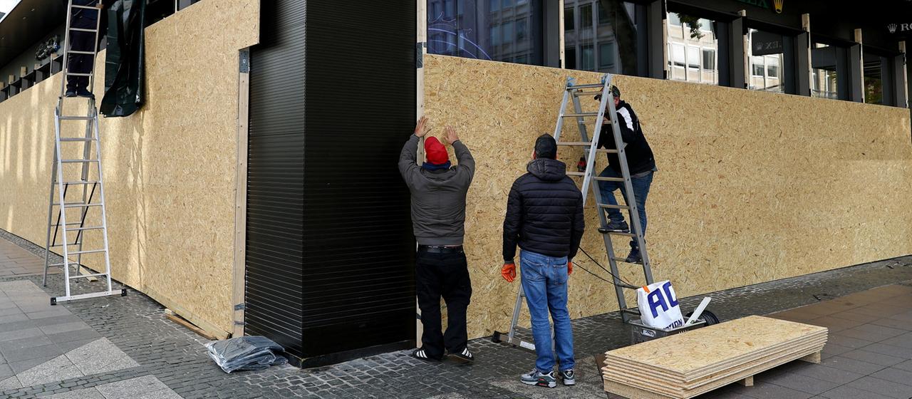 Mitarbeiter sichern ein Geschäft in Frankfurt am Main mit Holzbrettern ab.
