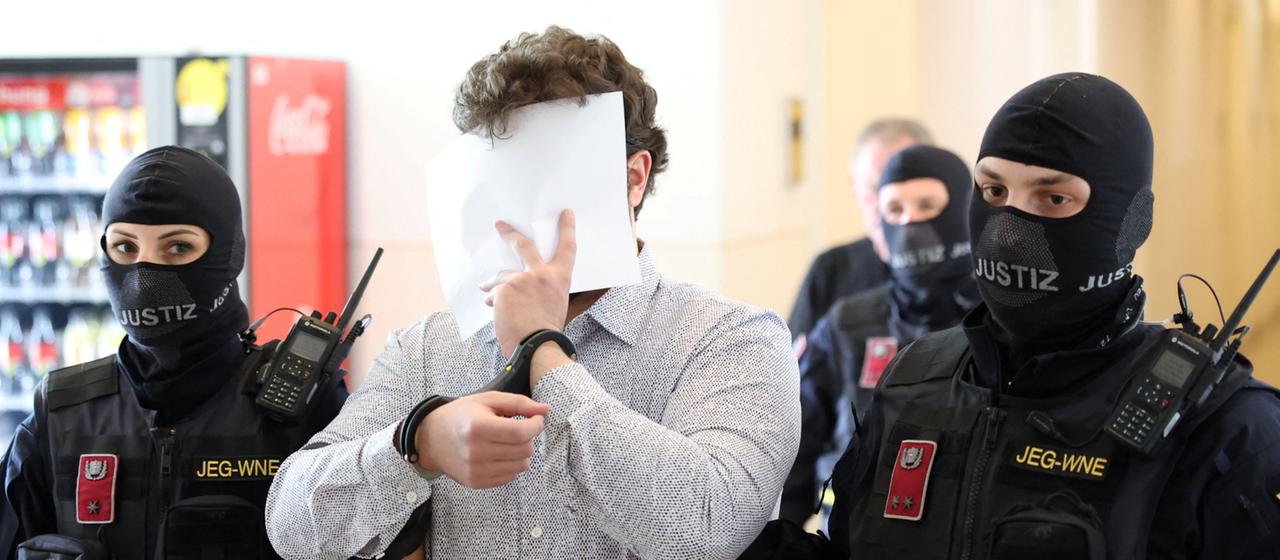 Beran A. wird von Sicherheitskräften begleitet.