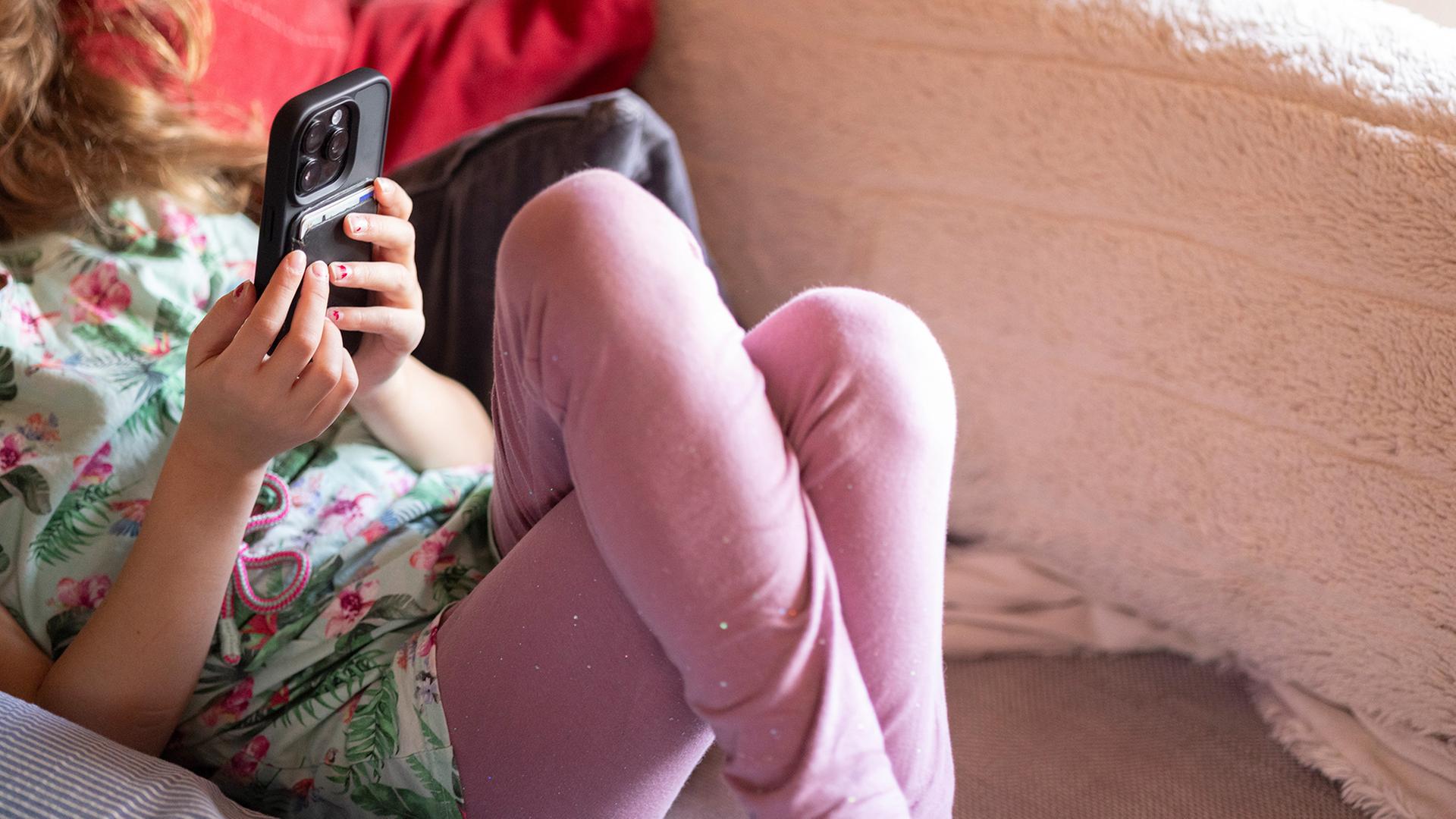 Ein Kind liegt mit einem Smartphone auf einem Sofa. | ARD-aktuell / Henning Retzlaff