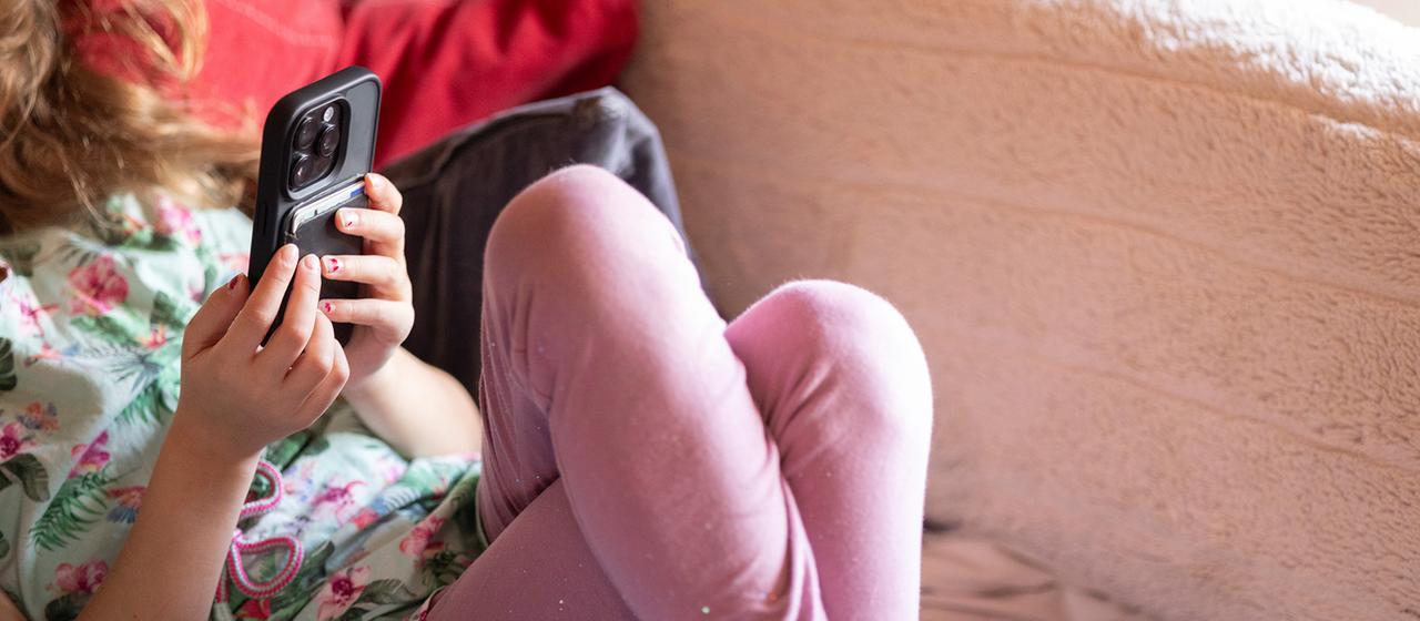 A child lies on a sofa with a smartphone.