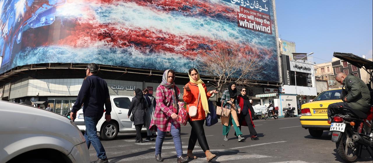 Passanten laufen in der iranischen Hauptadt Teheran an einer Plakatwand vorbei, die die US-Flagge zeigt.