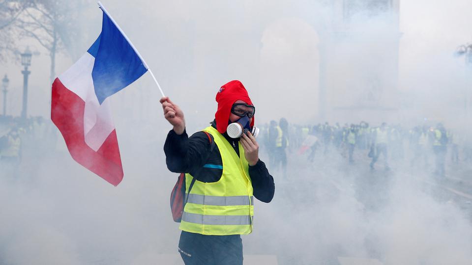 Demonstrant mit gelber Weste und französischer Flagge in Tränengaswolke