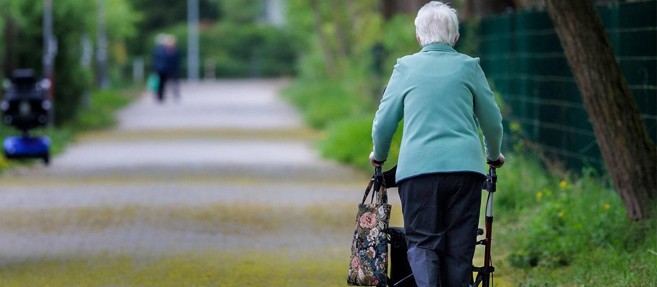 Seniorin mit Rollator in einem Park.
