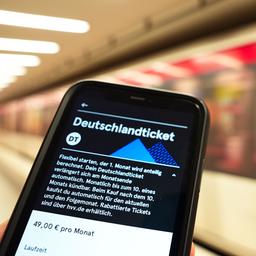 Ein Fahrgast hält ein Smartphone mit einem digitalen Deutschlandticket an einer U-Bahnstation in der Hand. 