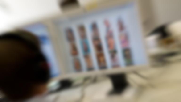 Ein Kriminialbeamter sitzt vor einem Bildschirm mit Fotos nackter minderjähriger Mädchen