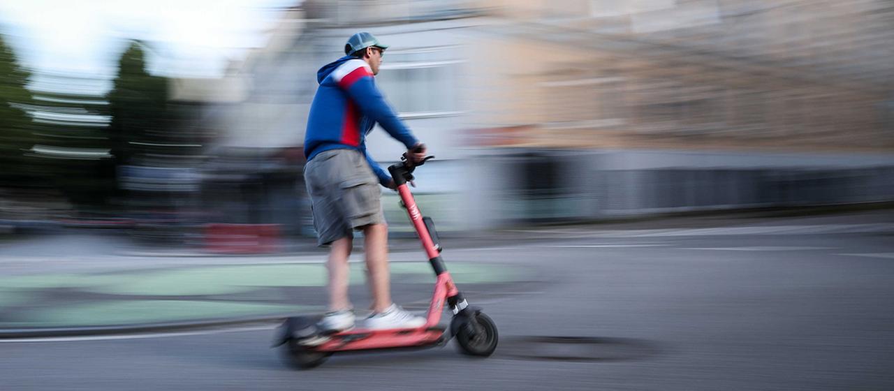 Ein Mann ist auf einem E-Roller unterwegs.