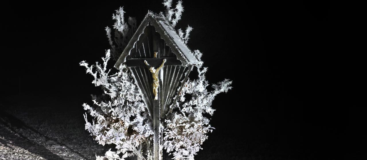 Ein Wegkreuz steht am frühen Morgen an einer Straße in Oy-Mittelberg im Allgäu im Raureif
