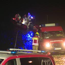 Einsatzkräfte stehen mit Einsatzwagen und einem Boot nachts am Rhein.