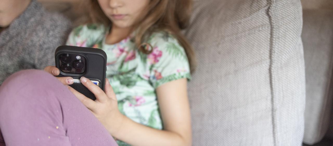 Ein sitzt mit einem Smartphone in der Hand auf dem Sofa.