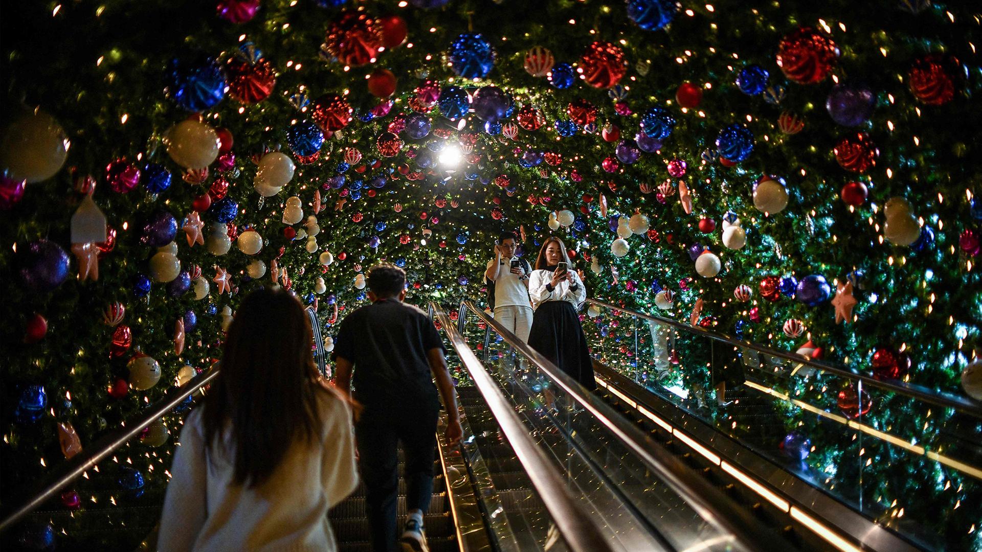 Menschen fahren auf einer Rolltreppe in einem Einkaufszentrum in Bangkok an Weihnachtsdekoration vorbei. | AFP