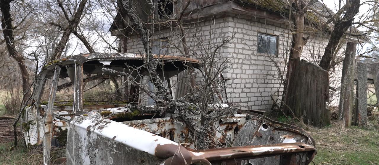 ein Haus und ein Autowrack in der Sperrzone von Tschernobyl