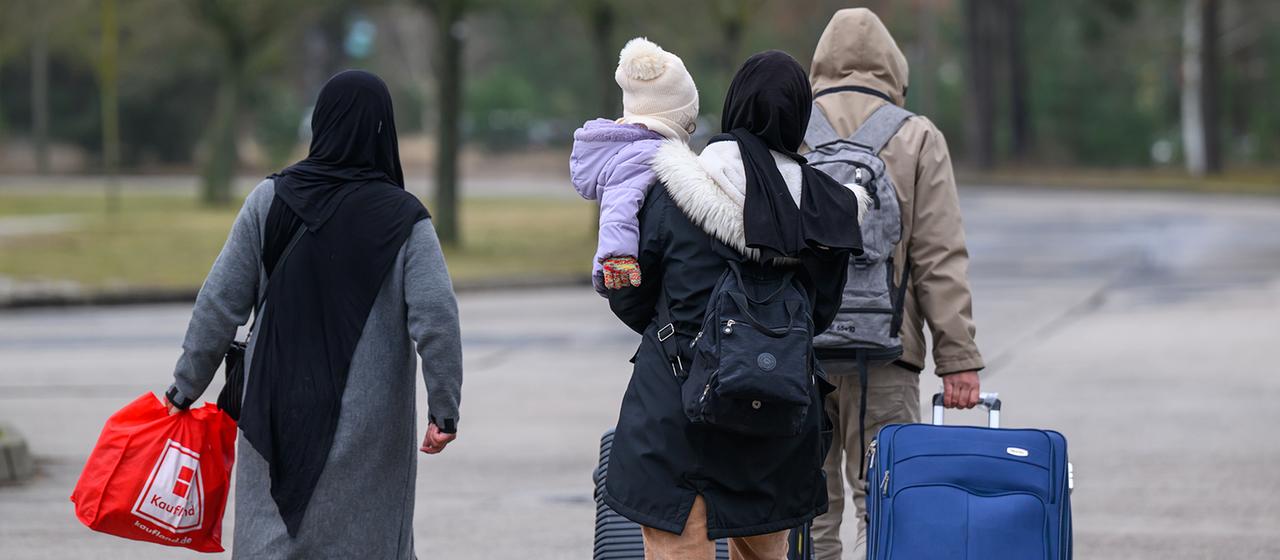 Migranten verlassen mit ihrem Gepäck das Gelände der Zentralen Ausländerbehörde Brandenburg (ZABH).