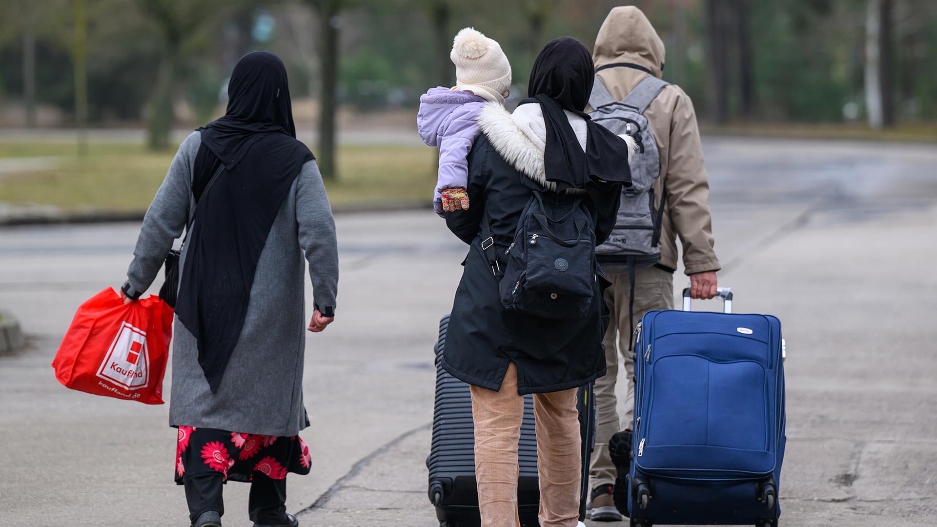 Migranten verlassen mit Reisegepäck das Gelände der Zentralen Ausländerbehörde Brandenburgs (ZABH). | dpa