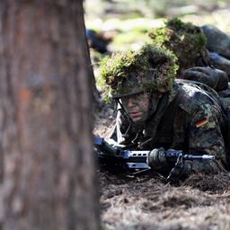 Soldaten in Tarnklamotten liegen zwischen Bäumen auf dem Waldboden. In ihren Händen halten sie Gewehre. Auf ihren Helme haben sie Pflanzen angebracht. (Symbolbild)