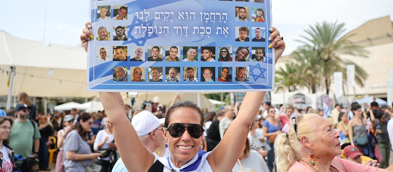 Eine Frau hält auf dem Geiselplatz in Tel Aviv ein Plakat mit Fotos von israelischen Geiseln. | EPA Eine Frau hält auf dem Geiselplatz in Tel Aviv ein Plakat mit Fotos von israelischen Geiseln.