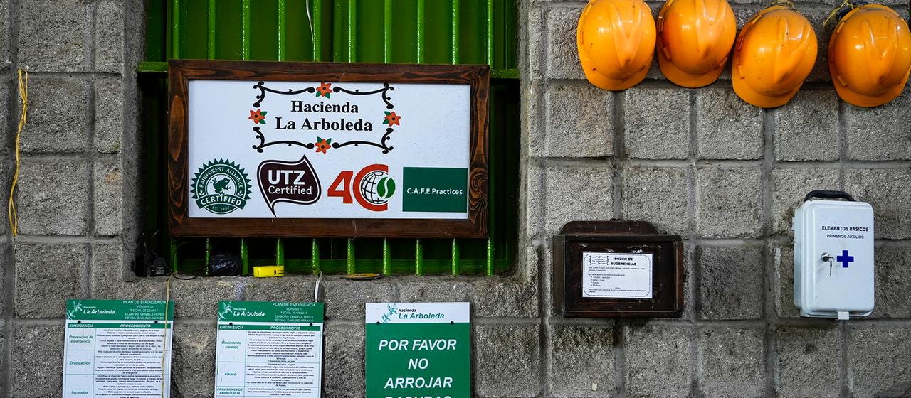 Hinweisschilder und Bauarbeiterhelme hängen an einer Wand. Ein Schild trägt die Aufschrift "Hacienda la Arboleda".