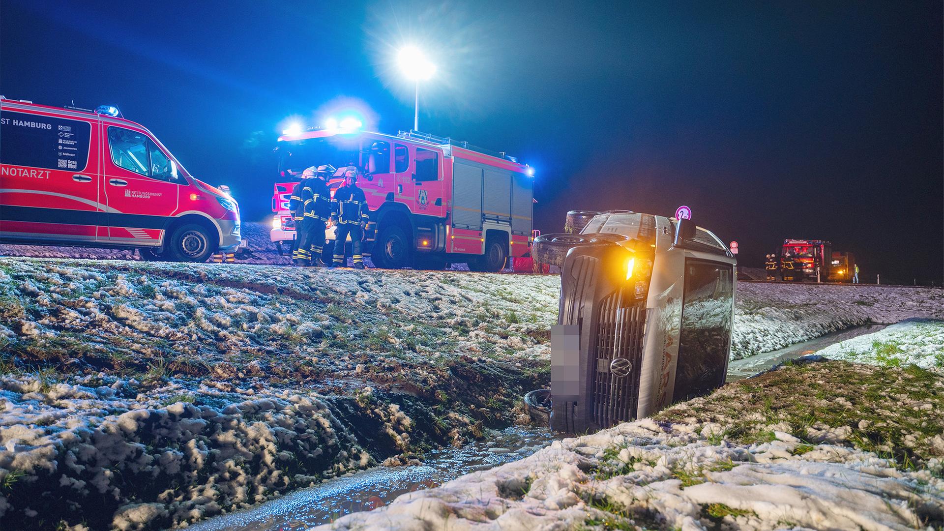 Ein LKW liegt in einem Graben am Rande einer schneebedeckten Straße, Feuerwehrleute sind im Rettungseinsatz.