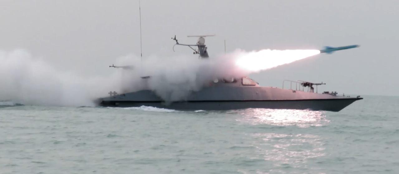 Ein Schiff feuert auf dem Wasser eine Rakete ab und wird von Rauch eingehüllt.