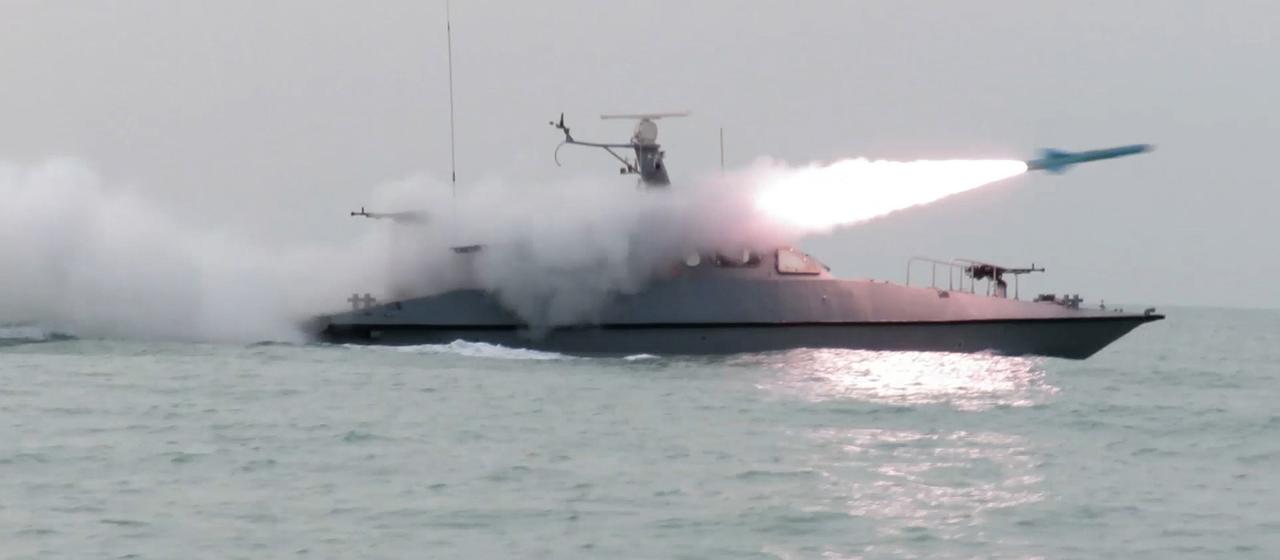 Ein Schiff feuert auf dem Wasser eine Rakete ab und wird von Rauch eingehüllt.