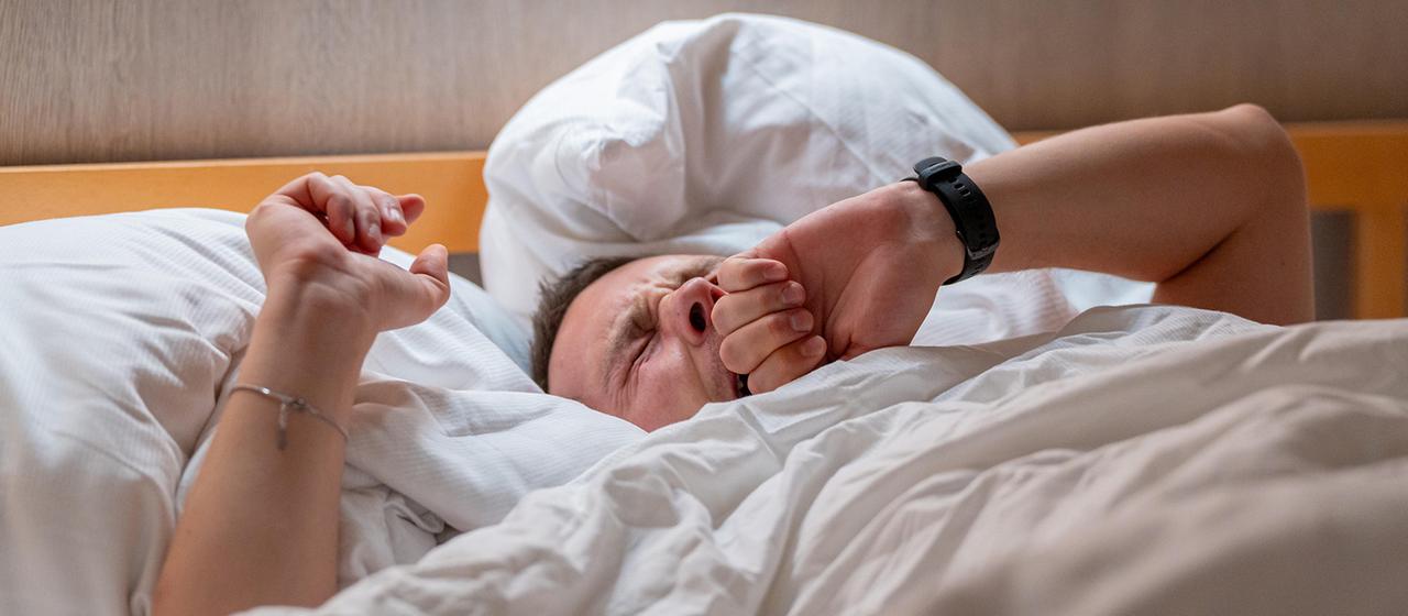 Ein Mann liegt gähnend im Bett.