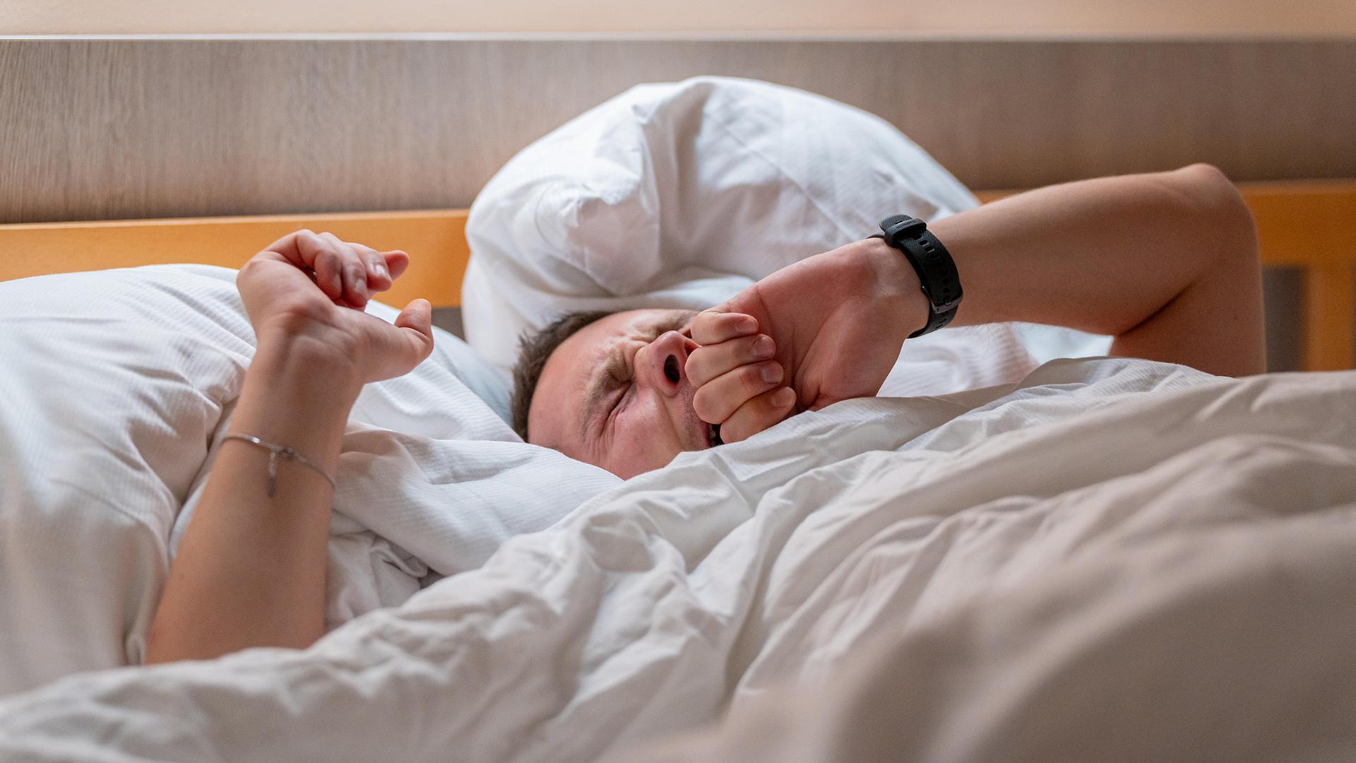 Ein Mann liegt gähnend im Bett. | picture alliance / CHROMORANGE