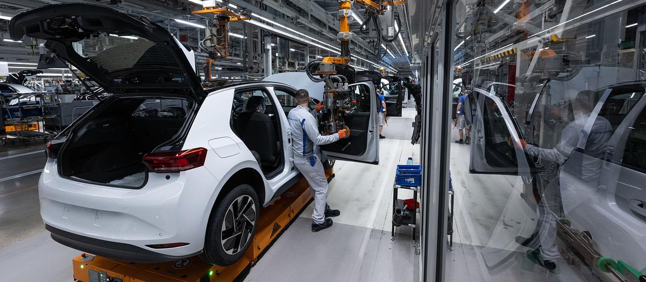Ein Arbeiter in einer Autoproduktion steht neben einem Auto und einem Roboterarm.