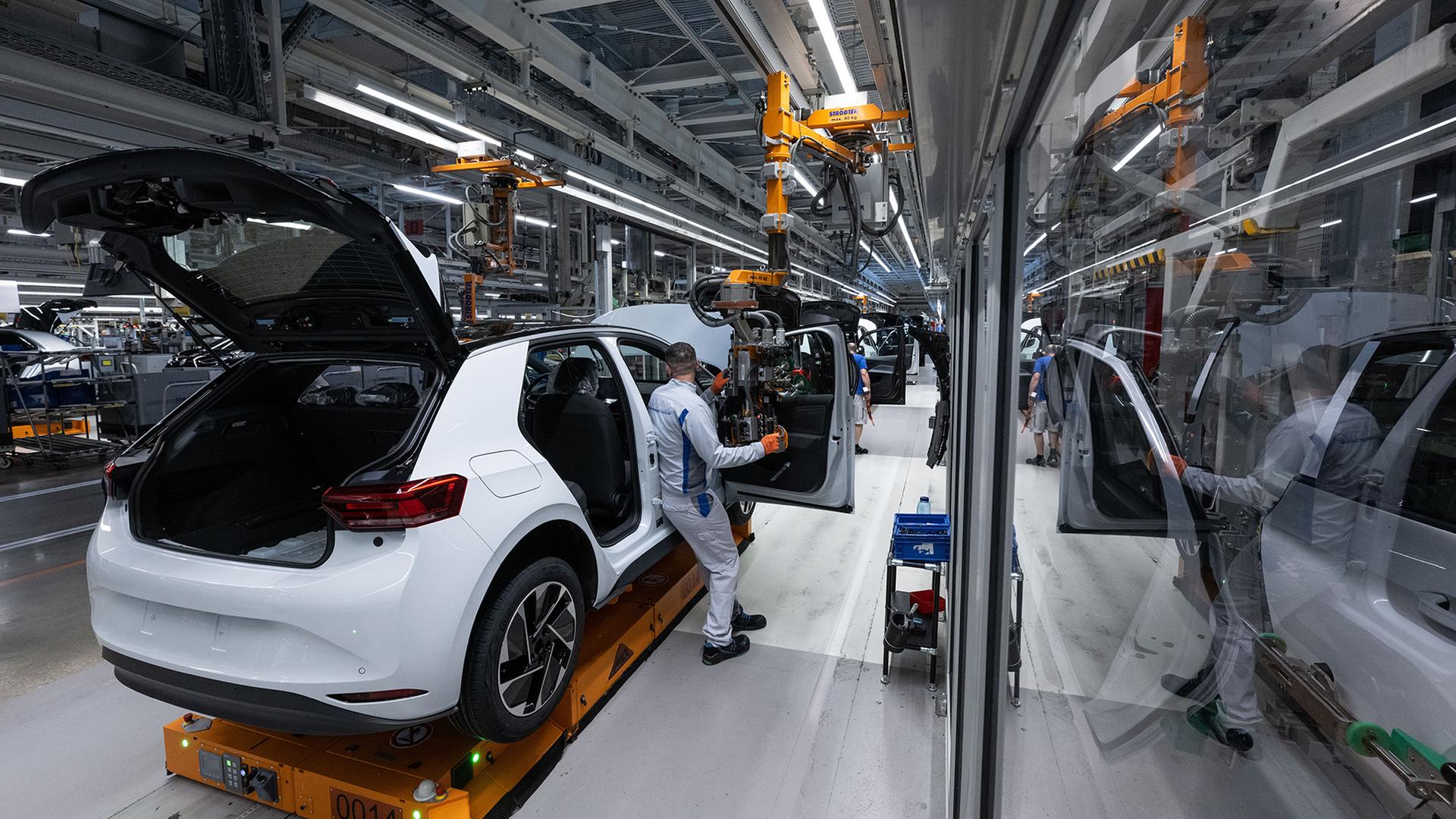 Ein Arbeiter in einer Autoproduktion steht neben einem Auto und einem Roboterarm. | dpa