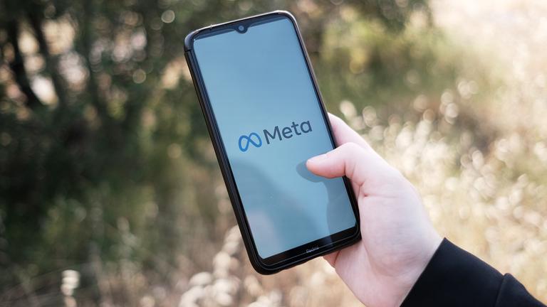 Eine Hand hält eine Smartphone, auf dem das Meta-Logo zu sehen ist.