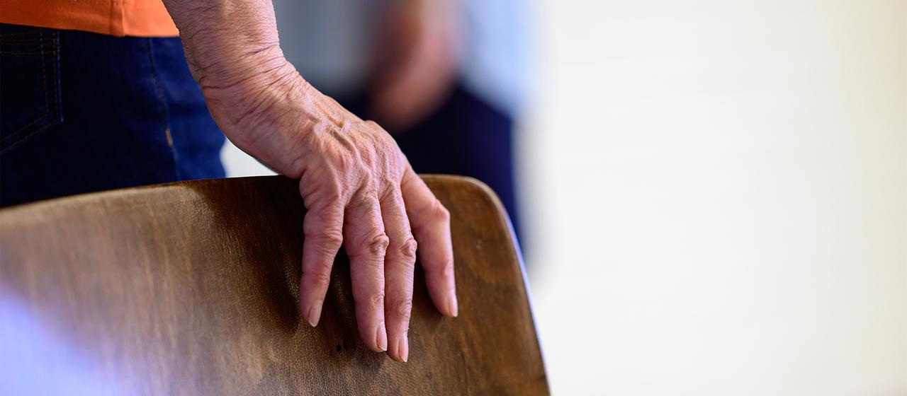 Eine alte Frau stützt sich auf einen Stuhl.