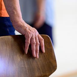 Eine alte Frau stützt sich auf einen Stuhl.