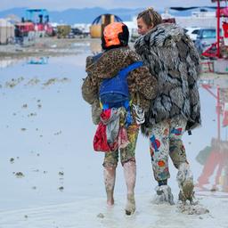 Menschen laufen im Matsch über ein Festivalgelände.