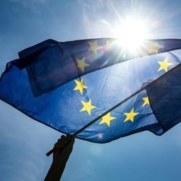 Eine Hand hält eine EU-Flagge und schwenkt sie gegen die Sonne.