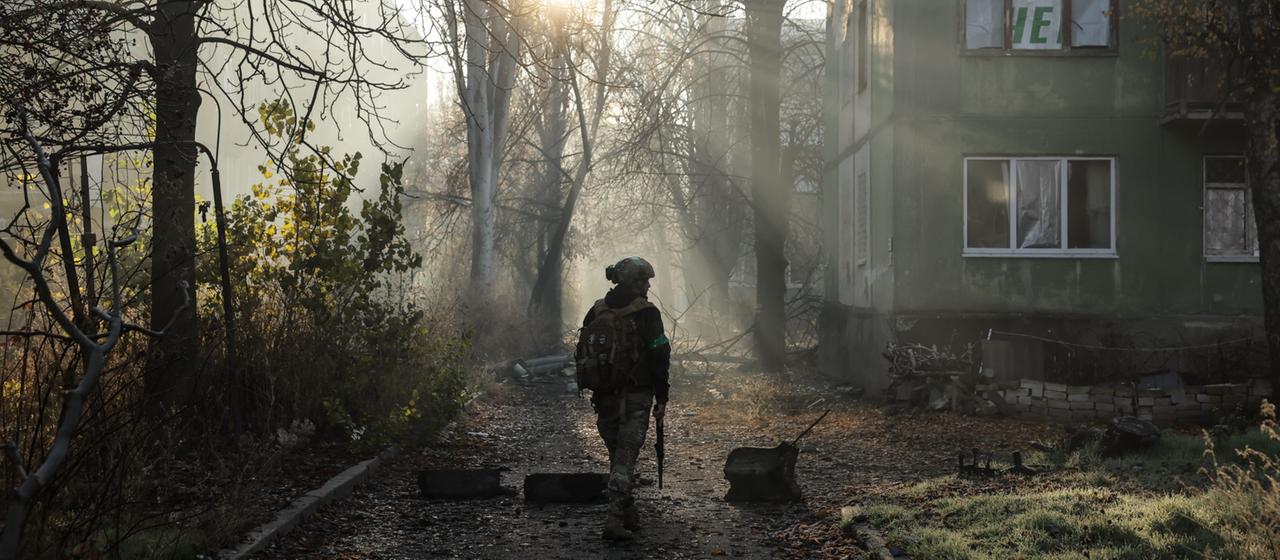 Ukrainischer Soldat vor Bäumen und Wohnhaus.