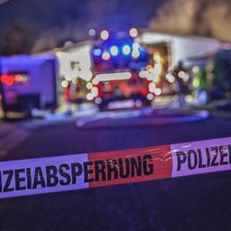 Absperrband mit "Polizeiabsperrung" im Vordergrund des Bildes. Im Hintergund, unscharf, Feuerwehr im Einsatz vor einem Gebäude.