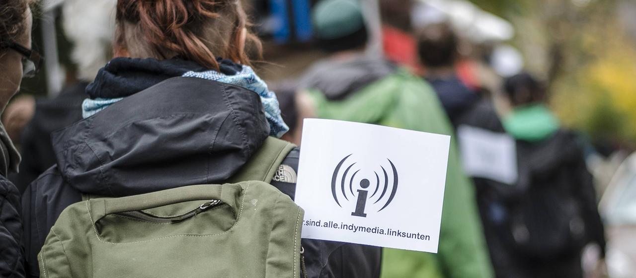 Eine Demonstrierende trägt ein Logo von "Indymedia linksunten" am Rucksack.