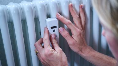 Eine Frau kontrolliert einen Heizkostenverteiler an der Heizung.