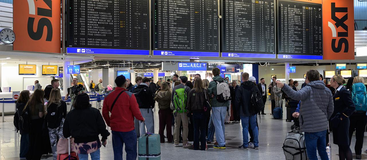 Menschen stehen vor einer Anzeigetafel am Frankfurter Flughafen.