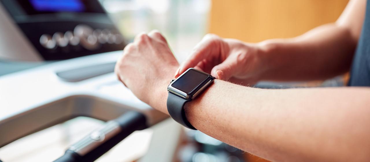 Eine Person auf einem Laufband bedient eine Smartwatch.
